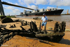 In a Tuesday June 18, 2913 photo, Savannah River scavenger Charlie Ellis searches for artifacts around the shipwreck called "Dave's Derelict" while a container ship passes beneath the Talmadge Memorial Bridge coming into port in Savannah. The rusted century-old tugboat with iron boiler, left, rises out of the water twice a day, when tides are low, a reminder of Georgia's lost maritime history. Some estimate around twelve-hundred historically significant ships dating to the early 1700s have gone down in Coastal Georgia waters. Not a single ship, though, has been excavated and put on permanent display. (AP Photo/Atlanta Journal-Constitution, Curtis Compton) MARIETTA DAILY OUT; GWINNETT DAILY POST OUT; LOCAL TV OUT; WXIA-TV OUT; WGCL-TV OUT AP